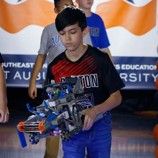Student carries a competition robot at a SCORE robotics tournament