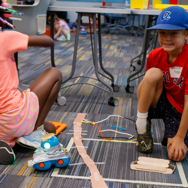 Young students work on a simple robotics activity on the floor during a S.C.O.R.E. summer camp