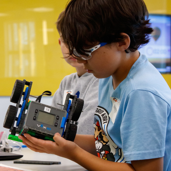Student examines a small wheeled robot during hands-on robotics instruction at a S.C.O.R.E. summer camp