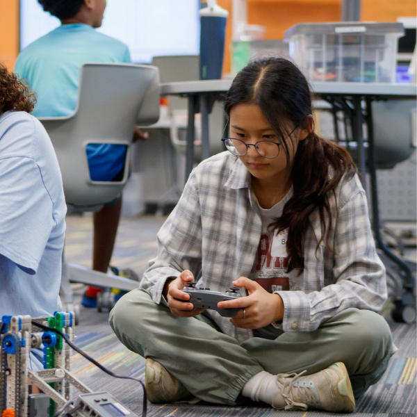Student programs a robot using a handheld controller during a S.C.O.R.E. summer camp activity